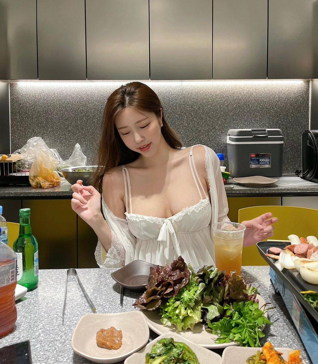 照片中的她正在吃烤肉，穿着白色睡衣大秀傲人身材。